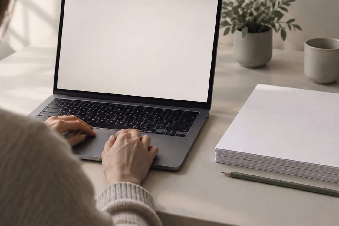 Hands on a laptop beside a stack of paper — the audit being written.
